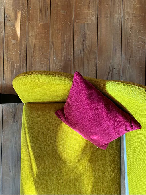 Gelbgrünes Sofa mit pinkem Kissen vor einer Holzwand